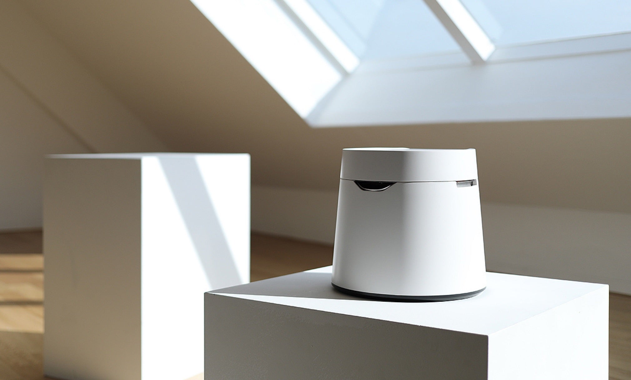 White smart home device on a white pedestal in a sunlit room with a skylight